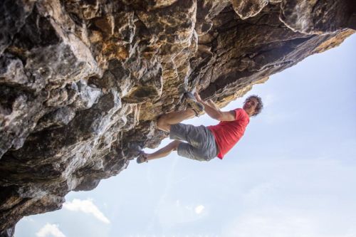 Adam Ondra leze po skále a usmívá se do kamery