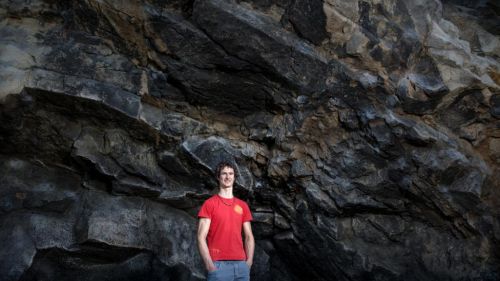 Adam Ondra stojí před skálou a má ruce v kapsách