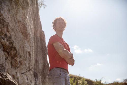 Adam Ondra stojí před skálou a má založené ruce