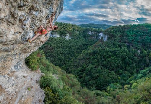 Adam Ondra leze na skálu, v pozadí je krásná zelená krajina