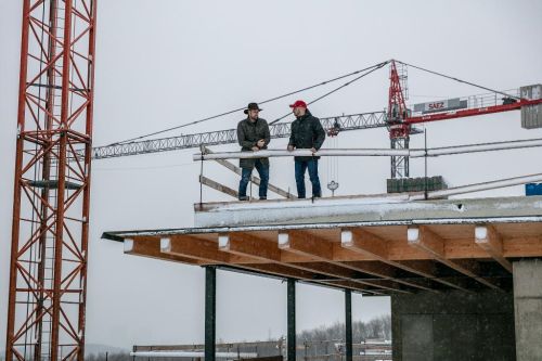 Martin Hubinger a Petr Teplý stojí na stavbě v zimě, za nimi je jeřáb