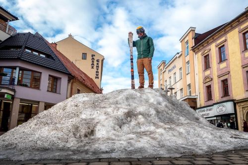 Ondřej Bank na kůpě sněhu ve městě s lyžemi a helmou