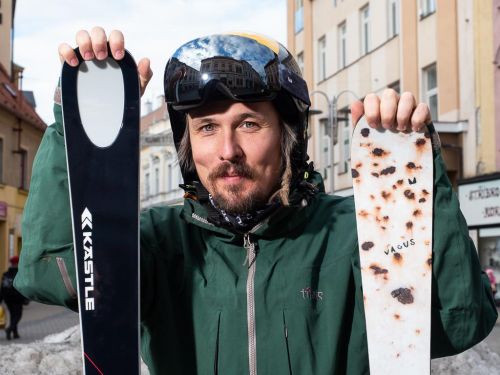 Ondřej Bank stojí ve městě, má na sobě helmu a drží lyže