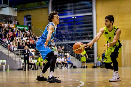 Zurab Kereselidze při basketbalovém zápase s míčem a soupeřem v basketbalové hale, v hledišti jsou diváci